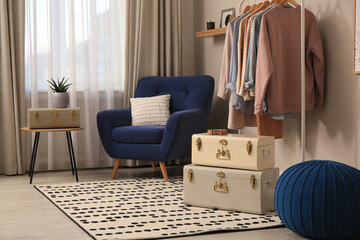 Stylish room interior with comfortable armchair, clothes and storage trunks