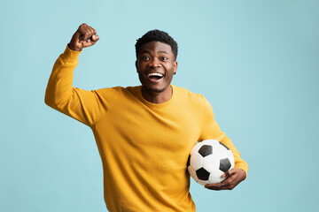 Emotional black guy with soccer ball posing on blue