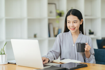 Portrait of young businesswoman sitting in office in front of computer and taking notes in notebook.Girl writer works on book,journalist writes article.Freelancer works remotely.