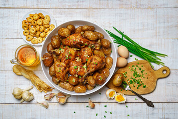 tasty lunch in rural style, healthy food - glass of beer, fried chicken meat and potatoes, garlic and green onions, cheese, boiled eggs and salt, cooked food on a white wooden boards