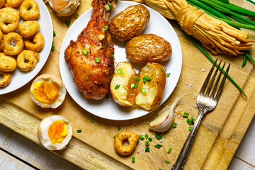tasty and healthy food, lunch in rural style - fried chicken meat and unpeeled potatoes, eggs, green leek, salt and garlic, cooked food on a wooden kitchen board