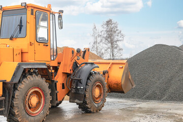 The front loader picks up gravel or crushed stone in the front bucket. Heavy construction machinery at the construction site. Transportation of materials at a concrete plant.