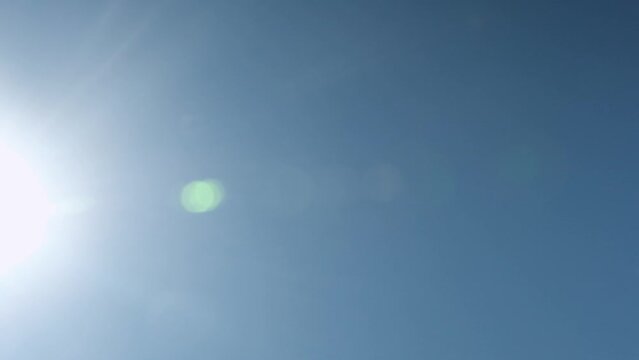 Airdrop of silver balloons attached to gift box at bright sunlight. Inflatable balls fall down against blue sky lit by sun rays. Low angle shot super slow motion