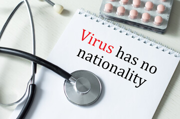 Virus has no nationality text on a notepad on the table next to a stethoscope and tablets in plates