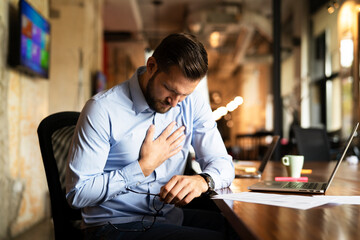 Young businessman having chest pain. Man sitting in the office working on laptop..