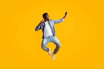 Fototapeta na wymiar Joyful black guy having fun, taking selfie on smartphone