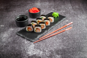 Assorted Japanese sushi on a black board with soy sauce, ginger, wasabi on a gray dark background