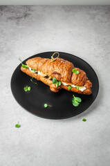 Croissant with vegetables and ham on a black platter on a gray light background