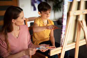 Mother and son painting at home. Little boy drawing with mom in living room.