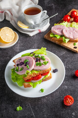 Breakfast with ham and greens sandwiches on a dark gray background with tea and lemon