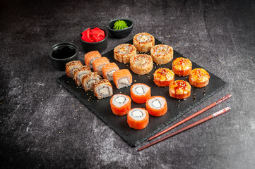 Assorted Japanese sushi on a black board with soy sauce, ginger, wasabi on a gray dark background