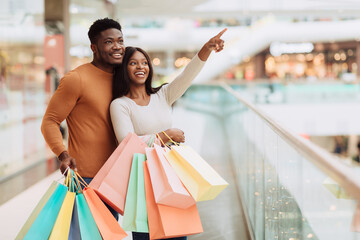 Portrait of black couple with shopping bags pointing at window