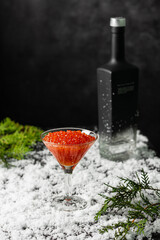 Red salmon caviar in a martini glass on and a bottle of vodka in the snow. Copy spase