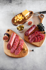 Meat plate with smoked delicacies, cheese, figs, grapes and olives, on wooden boards and gray background