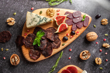 Cheese and meat plate with basil, nuts on a dark gray background