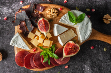 Cheese and meat plate with basil, nuts on a dark gray background