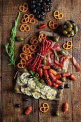 Smoked sausage on a dark wooden board, with olives, grapes and snacks