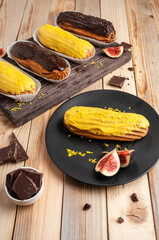 Eclairs with icing and cream, decorated with sprinkles and figs, on a wooden background
