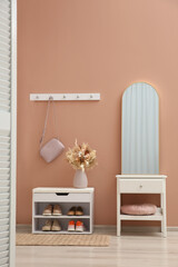 Hallway interior with mirror and white furniture near light pink wall. Stylish accessories