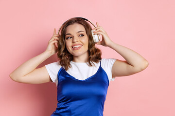 Happy young beautiful girl with long curly hair listening to music isolated on pink background. Concept of emotions, beauty, fashion. Trendy colors