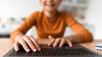 Smiling caucasian teen girl typing on laptop keyboard in kitchen interior, blurred, cropped
