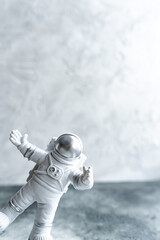 Trendy Miniature astronaut in spacesuit, peeking around corner waving his hand on gray textured background, vertical, copy space. World Day Cosmonautics. Science and space exploration, future.
