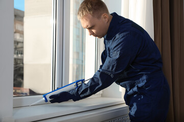 Construction worker sealing window with caulk indoors