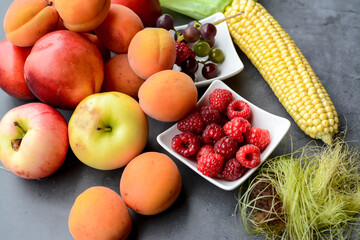 Sweet corn, apples, apricots and other berries and fruits on dark stone table