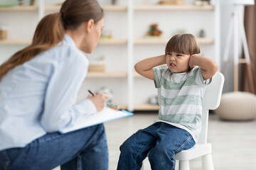 Professional psychotherapist trying to talk to difficult kid, grumpy little boy covering ears and...