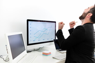 young man in front of the computer with pink jacket celebrating professional promotion with cheerful gesture
