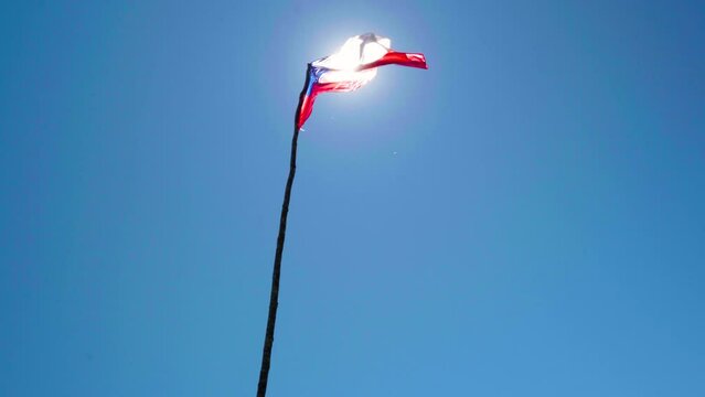 Handheld of sun beams shining through chilean flag hoisted on a pole and waving in the wind at daytime