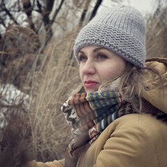 Portrait of a woman in nature, dry grass around, cold season. The girl is tense, anxiety in her eyes. Experiences, internal, psychological problems. Simple clothes, casual style.