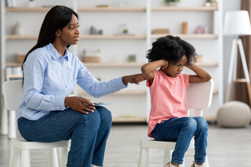 Worried black woman psychotherapist talking to unruly little girl