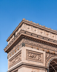 Partial view of the upper left of the Arc de Triomphe in Paris with a clear blue sky.