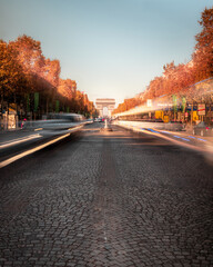 Beautiful view of the Arc de Triomphe in Paris in the middle of the Champs Elysées road while vehicles drive along the sides leaving trails in their wake.