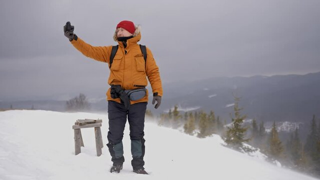 Man blogger takes a photo on the top of the mountain in heavy snowy weather