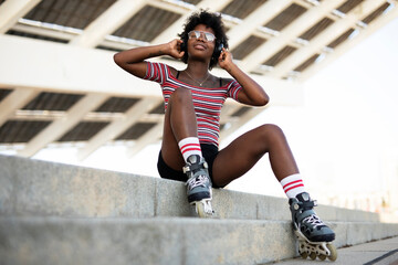Obraz na płótnie Canvas Beautiful African woman with roller skates. Urban sexy girl listening the music
