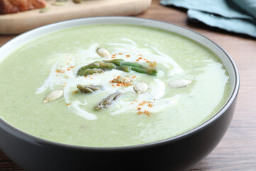 Delicious asparagus soup with pumpkin seeds on table, closeup