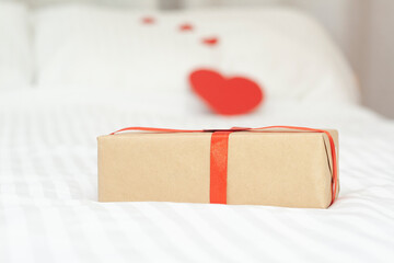 A gift on a white background. A gift on the bed. Hearts in the background.