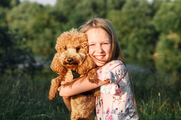 Poodle dog and his owner child. Adorable puppy and little girl hug having fun in park, copy space