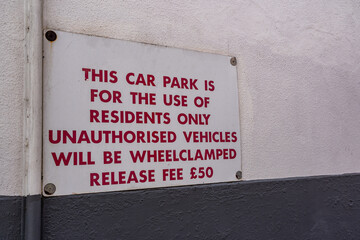 Warning sign outside of a private car park for residents of the building only. Wheel clamping and a fine for release are in operation if people break the rules