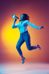 Fototapeta na wymiar Full-length portrait of happy young beautiful girl with long curly hair jumping isolated on orange background in neon light, filter. Concept of emotions, beauty, fashion