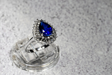 white gold jewelry ring with a large blue pear-cut sapphire and diamonds on a gray background