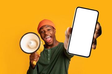 Excited black guy shouting into megaphone, showing big smartphone with empty screen, offering mockup space for ad - obrazy, fototapety, plakaty