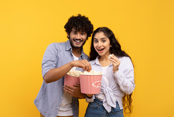 Amazing entertainment, leisure time together. Surprised indian guy and lady eating popcorn and watching movie