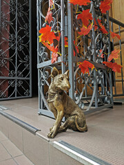 Bronze statue of a sitting bull terrier at a metal decorative door, decorated with autumn leaves