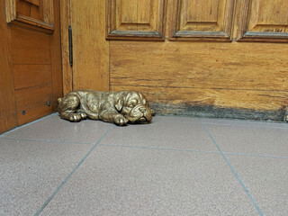 Bronze statue of a sleeping bulldog puppy lies at the wooden door as a decor
