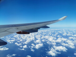 View from the porthole on the wing of an airplane with a red aircraft engine flying over beautiful white clouds and the sea.