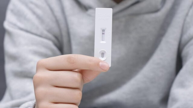 Coronavirus pandemic protection. Teenager using rapid antigen test kit for self test at home. Kid hand showing Covid-19 negative test result on test strip