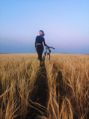 A girl with a bicycle stands in the middle of a wheat field. concept nature, freedom, sport